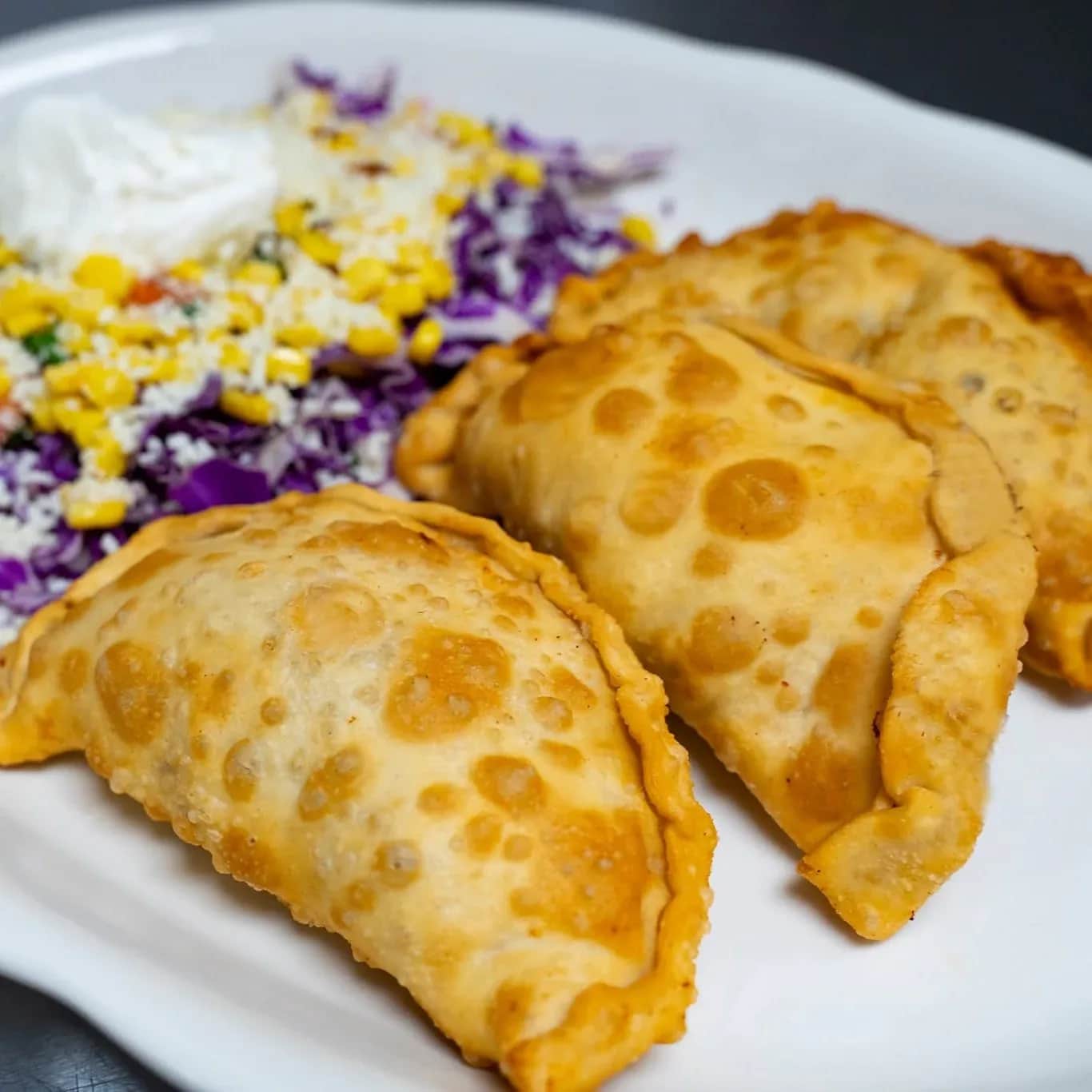 Three crispy empanadas served with red cabbage, roasted corn, sour cream, and pico de gallo