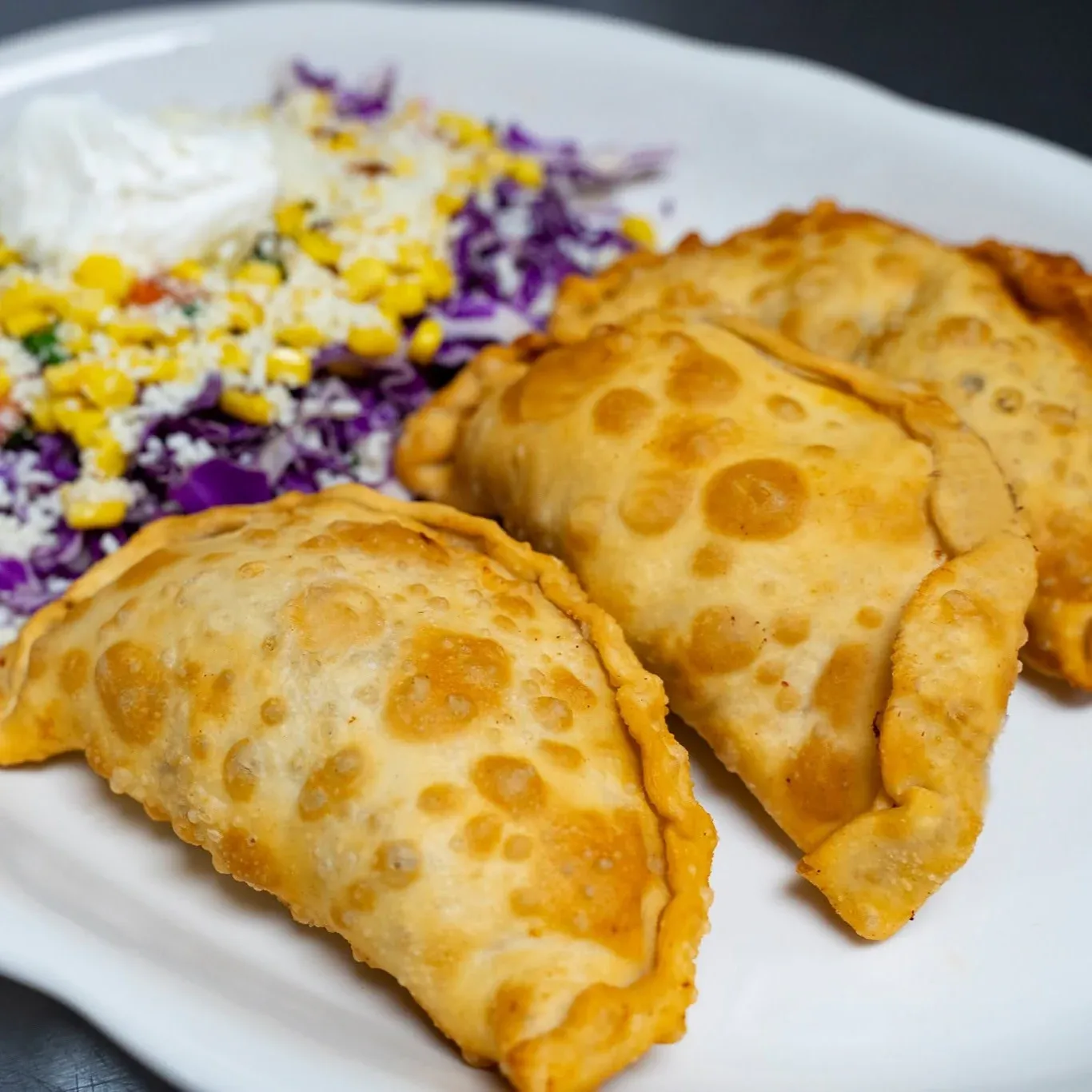 Three crispy empanadas served with red cabbage, roasted corn, sour cream, and pico de gallo